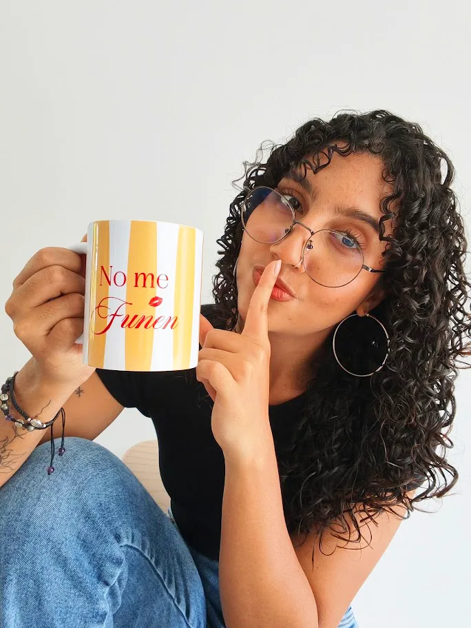 Andy sosteniendo un mug personalizado, con el dedo en los labios